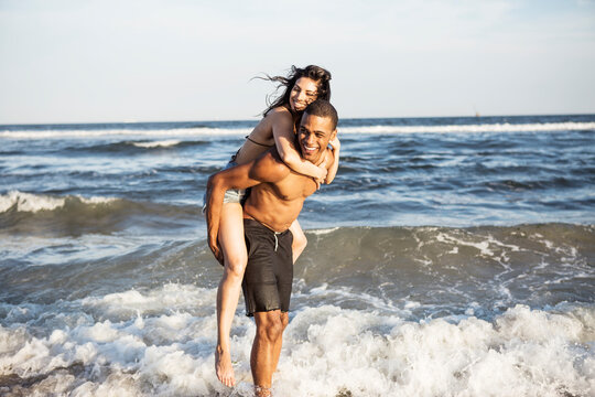 Couple enjoying piggyback ride at shore against sea