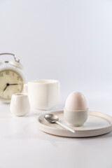 White egg with white plates, cup and alarm clock over white background for breakfast