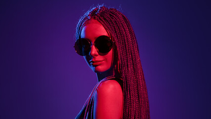 Young girl with dreadlocks hairstyle and sunglasses. Multi-colored saturated light.