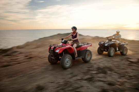 Couple riding quad bikes on beach against sky