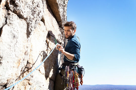 Man looking at climbing rope while rock climbing against clear sky