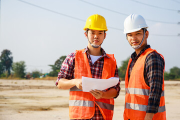 Portrait of Two Engineer, field engineer, foreman, owner standing in construction site project and Electric power line and pole in background. Asian engineer. High voltage power line pylon.