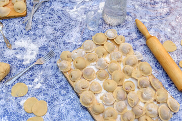 Preparation of Russian dumplings Pelmeni, Siberian food. Group of dumplings lie on a wooden board next to the rolling pin and decanter of vodka. Top view. Selective focus