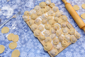 Preparation of Russian dumplings Pelmeni, Siberian food. Prepared pieces of dough lie on a table strewn with flour. Next to the rolling pin on a wooden board there are ready-made dumplings.
