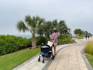Woman and newborn child in a stroller are walking in the park