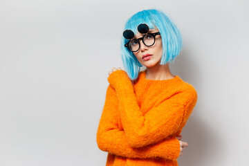 Portrait of fashionable young girl with blue hair wearing orange sweater and round glasses against white background.