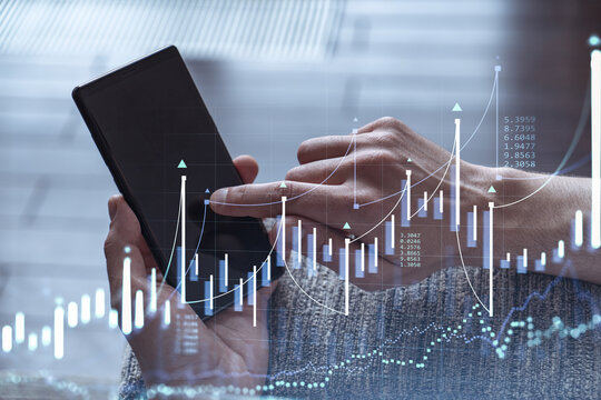 Trader holding in the hands a smart phone and researching stock market to proceed right investment solutions. Internet trading and wealth management concept. Hologram Forex chart over close up shot.