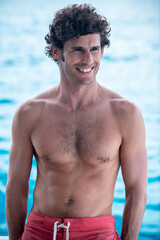 Obraz premium Portrait of handsome man, shirtless surfer with white teeth smile and blue ocean on background in Maldives