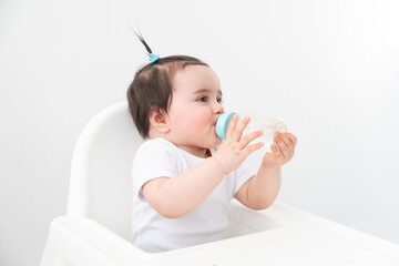 baby girl in baby chair drinking water from baby bottle on white background.