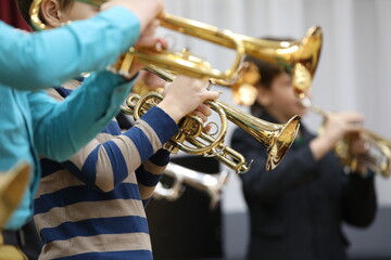 A group of school musicians plays wind instruments a golden shiny trumpet a flugelhorn while rehearsing indoors