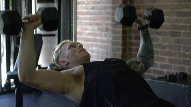 Tattooed man in home gym close up doing incline dumbbell chest press