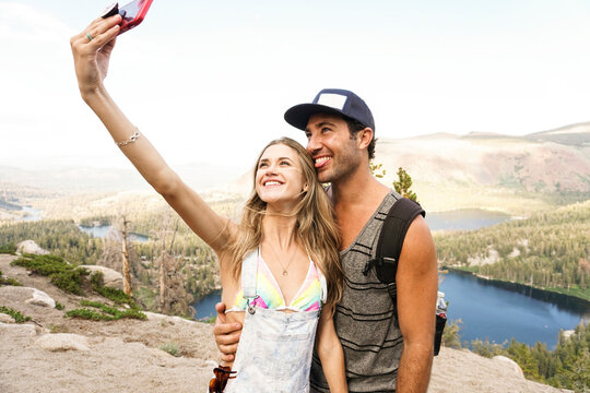 Happy couple taking selfie with mobile phone while standing on mountain against sky