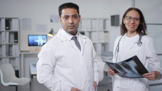 Medium portrait of two lung specialists standing together in doctors office, working with X-ray picture then looking at camera