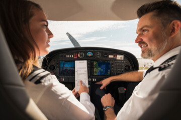 Rear view of female trainee discussing paper with male pilot in airplane at airport