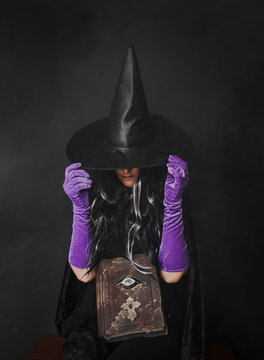 Woman dressed in witch costume sitting against black background during Halloween