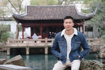 one Asian young man sitting in traditional Chinese garden, looking at camera