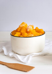 Frozen pieces of pumpkin in a white bowl with a wooden spatula on white table