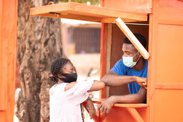 nigerian man in a kiosk and woman wearing face masks touch elbows