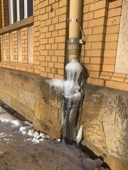 Wasserleitung draußen zugefroren mit Eis Schicht an Hauswand. Frost schaden Wasser Abflussrohr