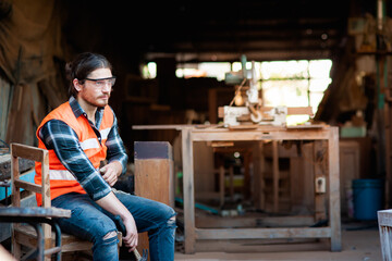 Handsome Caucasian male carpenter that serves to repair wood furniture With a hammer and chisel in hand, sitting on chair in the shop relax and resting