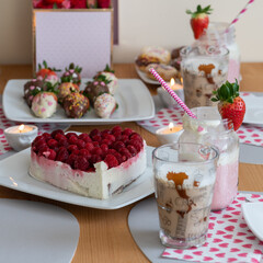 Ein bunt gedeckter Tisch mit Leckereien zum Nachtisch, Himbeer-Kuchen, Erdbeeren in der Schokolade und Milchshakes und Latte Macchiato. Frühling auf dem Tisch oder Valentinstag und Geburtstag.