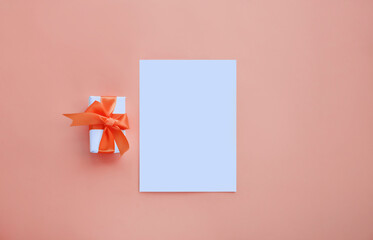 White invitation card mockup with small present box on peach background