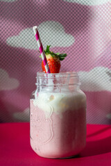 Nahaufnahme von einem Milchshake mit Erdbeeren und Himbeeren in einem vintage Glass. Pinkes Hintergrund mit weißen Wolken.