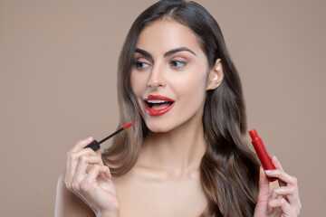 Long-haired woman painting lips with red gloss