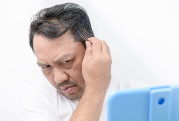 Fototapeta premium Asian middle man using tweezers to pluck his gray hair isolated