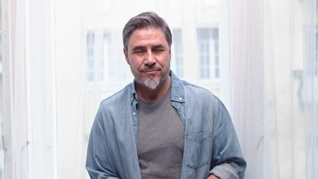 Portrait Of Middle Aged Grey Haired Man Standing In Window At Home, Smiling.