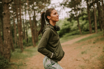 Young beautiful female runner listening to music and taking a break after jogging in a forest