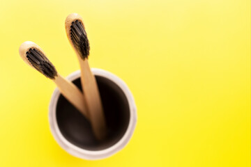 Organic bamboo toothbrushes in ceramic holder. Plastic free, eco friendly equipment for personal oral hygiene. Yellow background, top view.