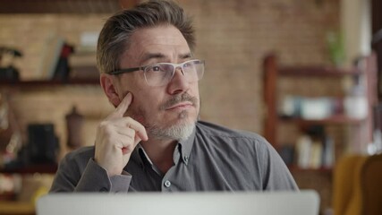 Older man working online with laptop computer at home sitting at desk. Home office, browsing internet, study room. Man thinking solving problem. - Powered by Adobe