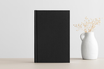 Black book mockup with a gypsophila decoration on the beige table.