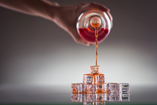 Pouring red drink over ice cubes; mixing drinks- conceptual image