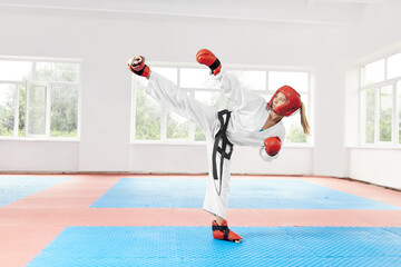 Sporty woman against big window showing martial art foot kick at fight class.