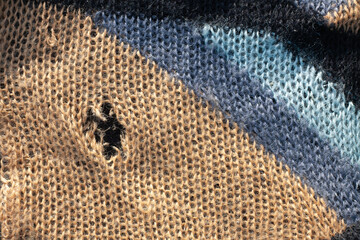 A hole in the knitted fabric. Background of woolen fabric with a hole.