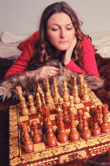 Portrait of a woman in a red dress with curly hair on the bed next to the chess set.
