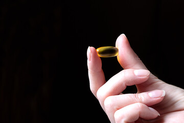 Human hand holds golden pill of omega 3. Healthy liife, woman health. Dark background