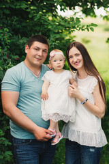 Family enjoying life together in the summer park. Happy young family outdoors. Mother, father are hugging their daughter outdoors and having fun in nature. The concept of family summer holiday