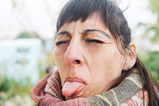 Portrait of woman eyes closed while sticking out tongue outdoors