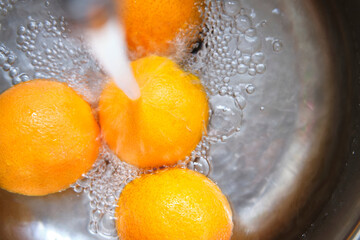 washing oranges under the tap in the metal kitchen sink