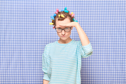 Disgruntled girl with bright hair curlers is gazing into the distance