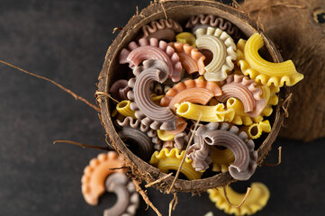 colored pasta in the form of handmade scallops in a coconut plate on a gray vintage background, top view