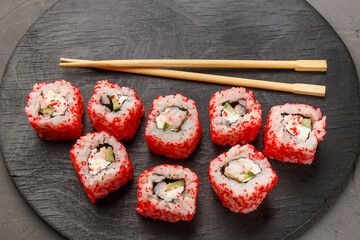 Roll with shrimp and tobiko caviar and sticks on a black round board on a gray background.