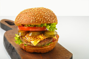 Classic burger with beef, cheese vegetables in sauce on a bun with sesame seeds on a wooden board with a handle on a white plate.