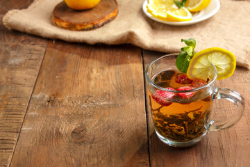 green tea in a glass cup with strawberries mint and lemon on a wooden table next to lemon in a plate on a napkin.