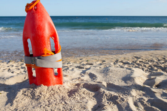 Orange rescue buoy planted on sand beach. Sea weaves as background