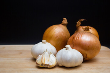 The yellow onions and garlics isolated black background on a wooden cutting board