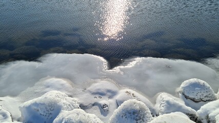 In the winter, the Baltic Sea and ice covered the frozen rocks at dawn. Baltic Sea - winter beach with frozen stones. The picturesque landscape of the Baltic Sea in the polar winter